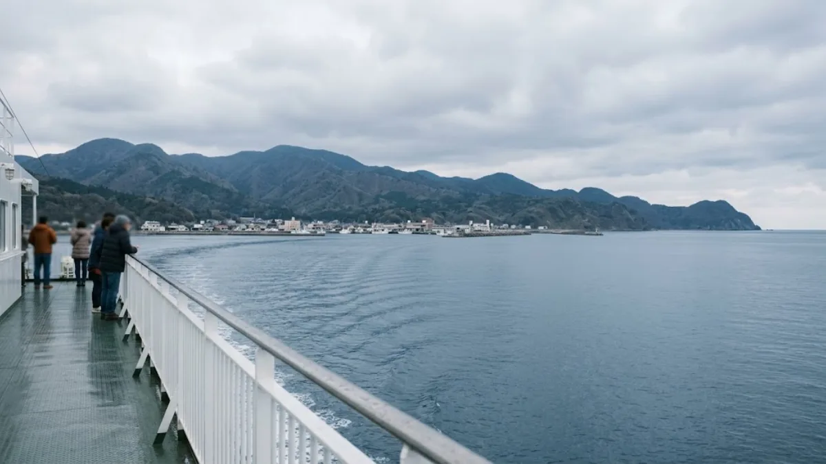 佐渡島へ向かうフェリーのデッキから見た穏やかな海と遠くの港町、離島への渡航を連想させる情景