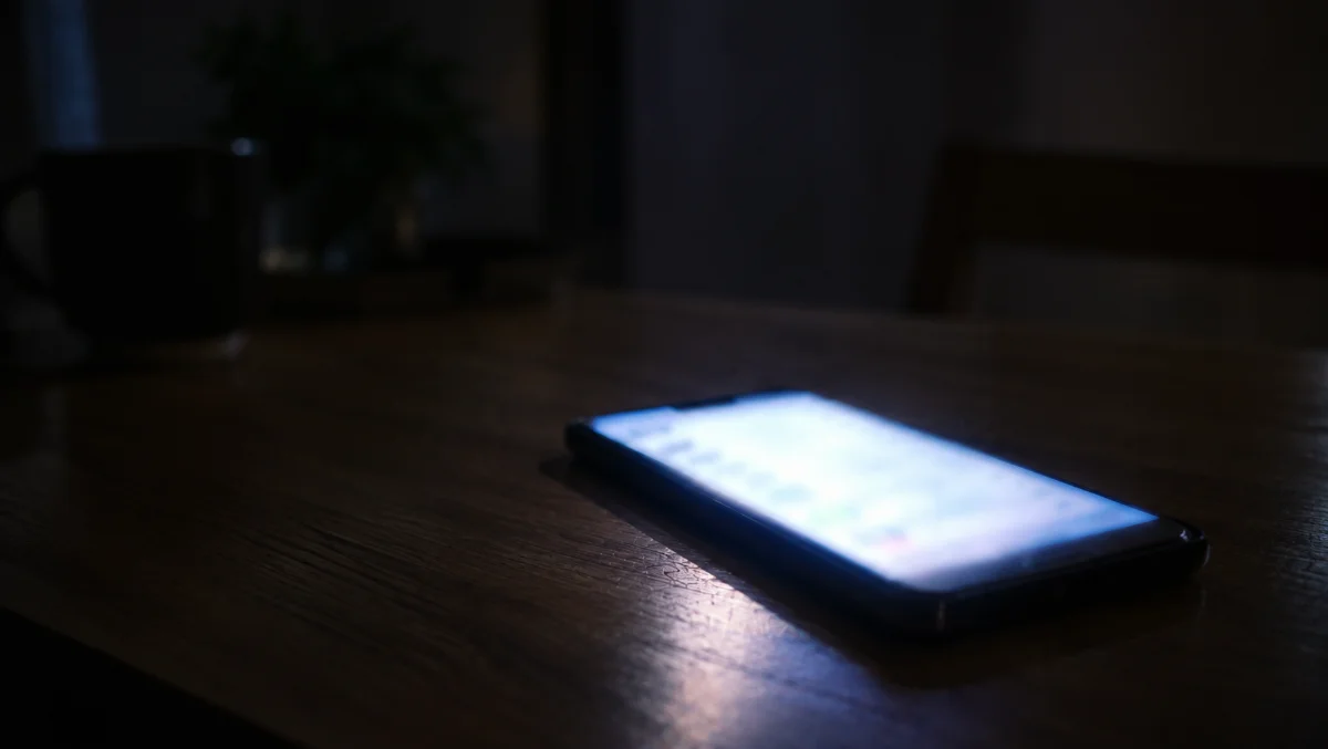 夜、スマートフォンのメッセージ画面の光だけが見える手元