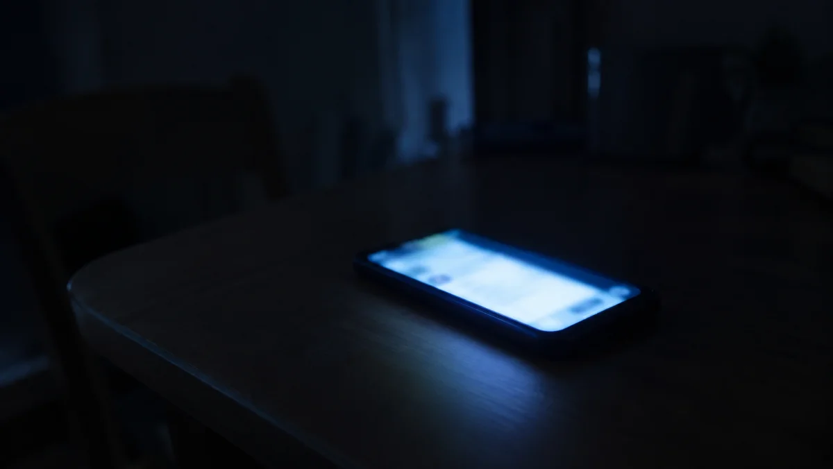 夜の暗い部屋でテーブルに置かれたスマートフォンの画面の光だけが周囲を照らしている情景